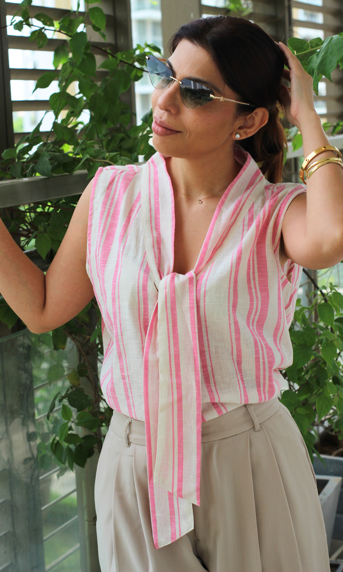Close-up of the tie-neck detail on a sleeveless pink and white striped cotton blouse, paired with neutral high-waisted pants.