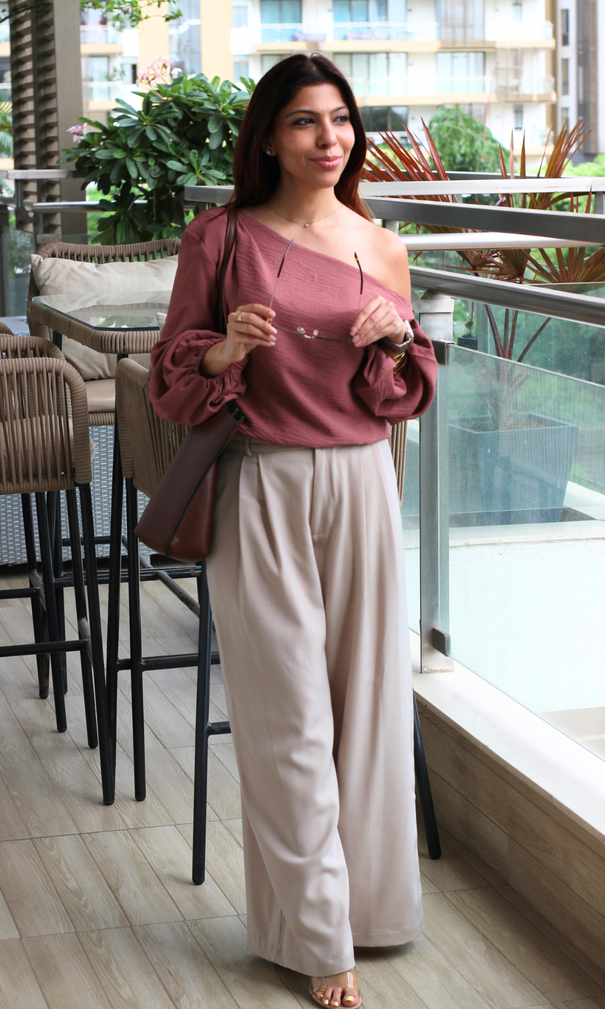 Effortless balcony look featuring a mauve off-shoulder top, cream wide-leg pants, sunglasses, and a brown sling bag.