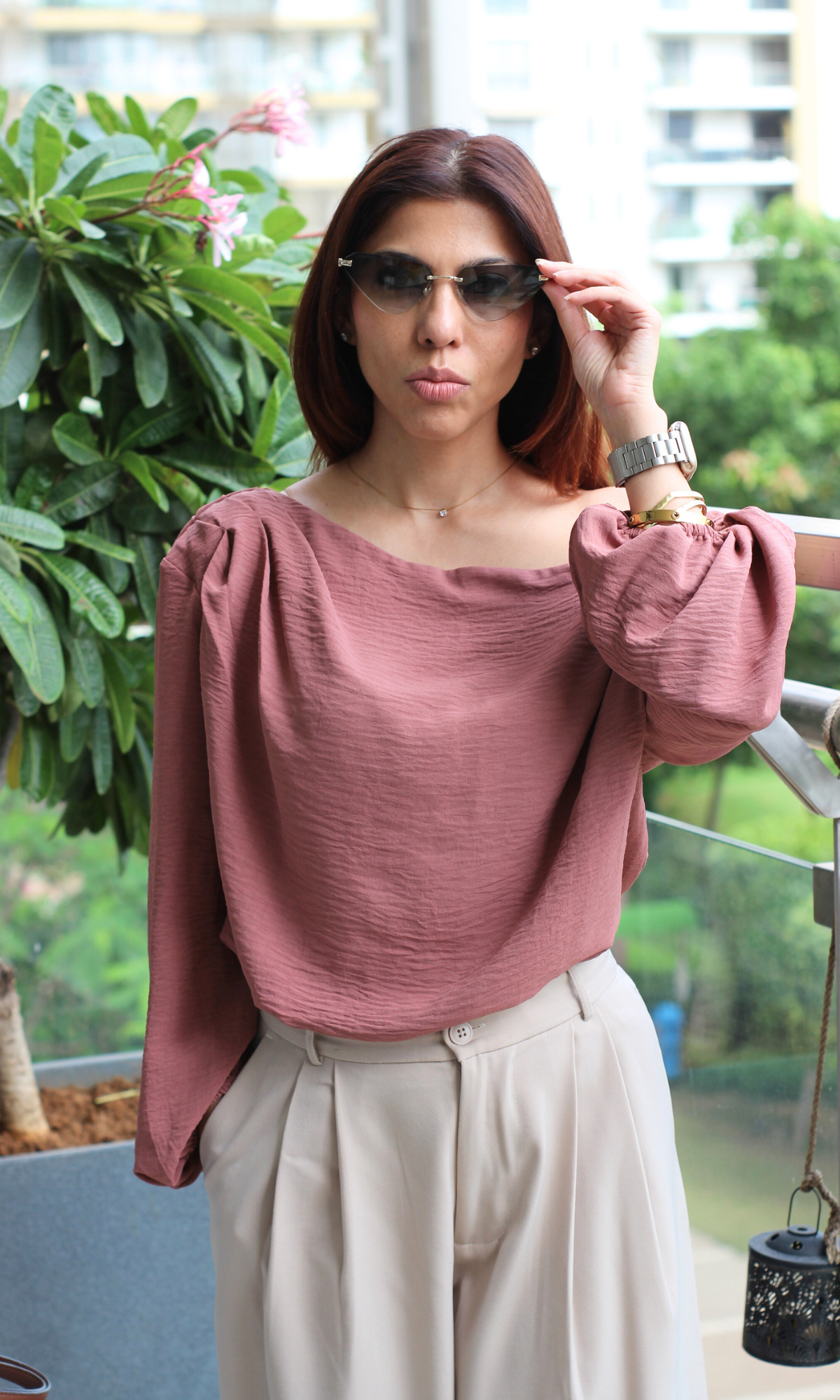 Chic mauve off-shoulder blouse styled with cream high-waisted pants and sunglasses on a balcony.