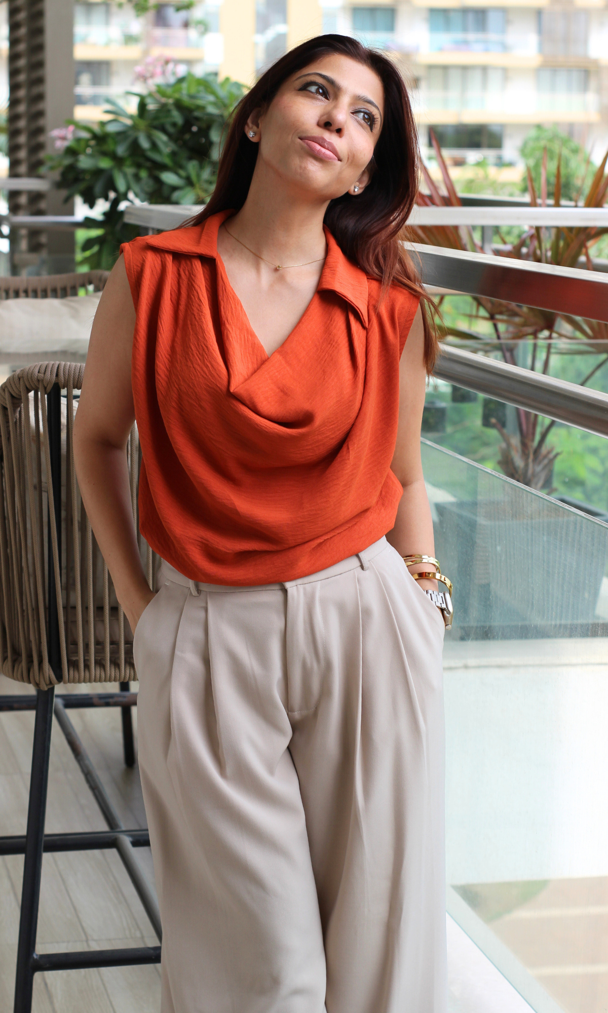 Sophisticated casual outfit: sleeveless draped rust blouse styled with pleated neutral trousers.