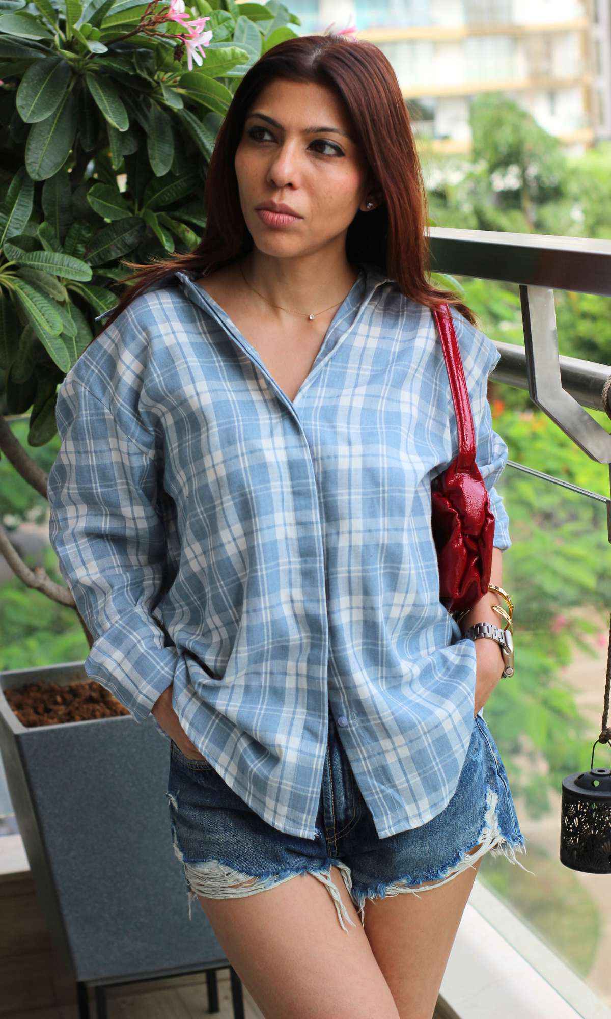 Lightweight blue plaid shirt with rolled sleeves paired with casual frayed shorts and a bright red shoulder bag for a pop of color.