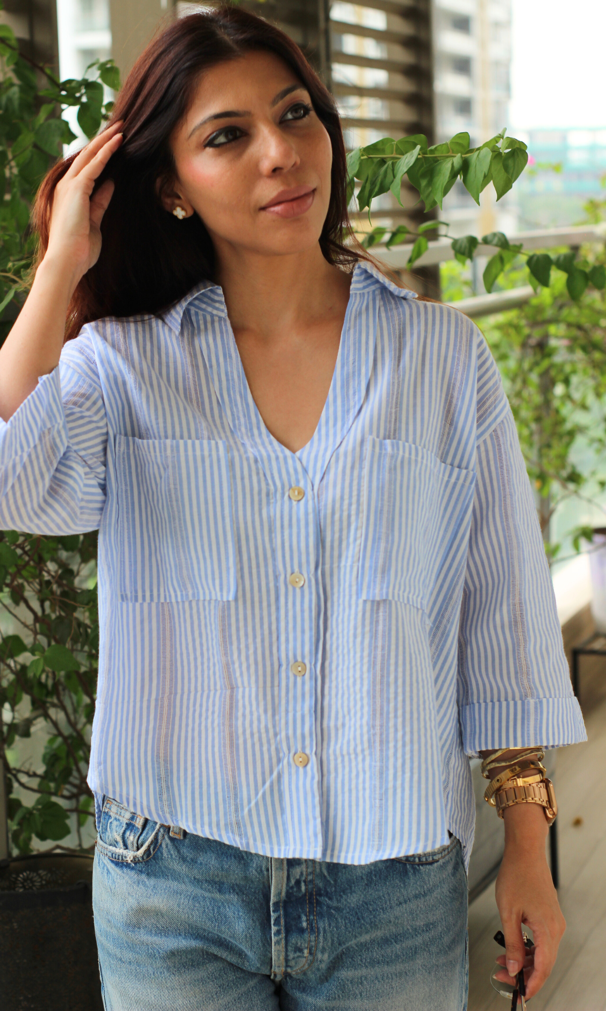 Striped blue button-down shirt with rolled sleeves, styled with relaxed denim.