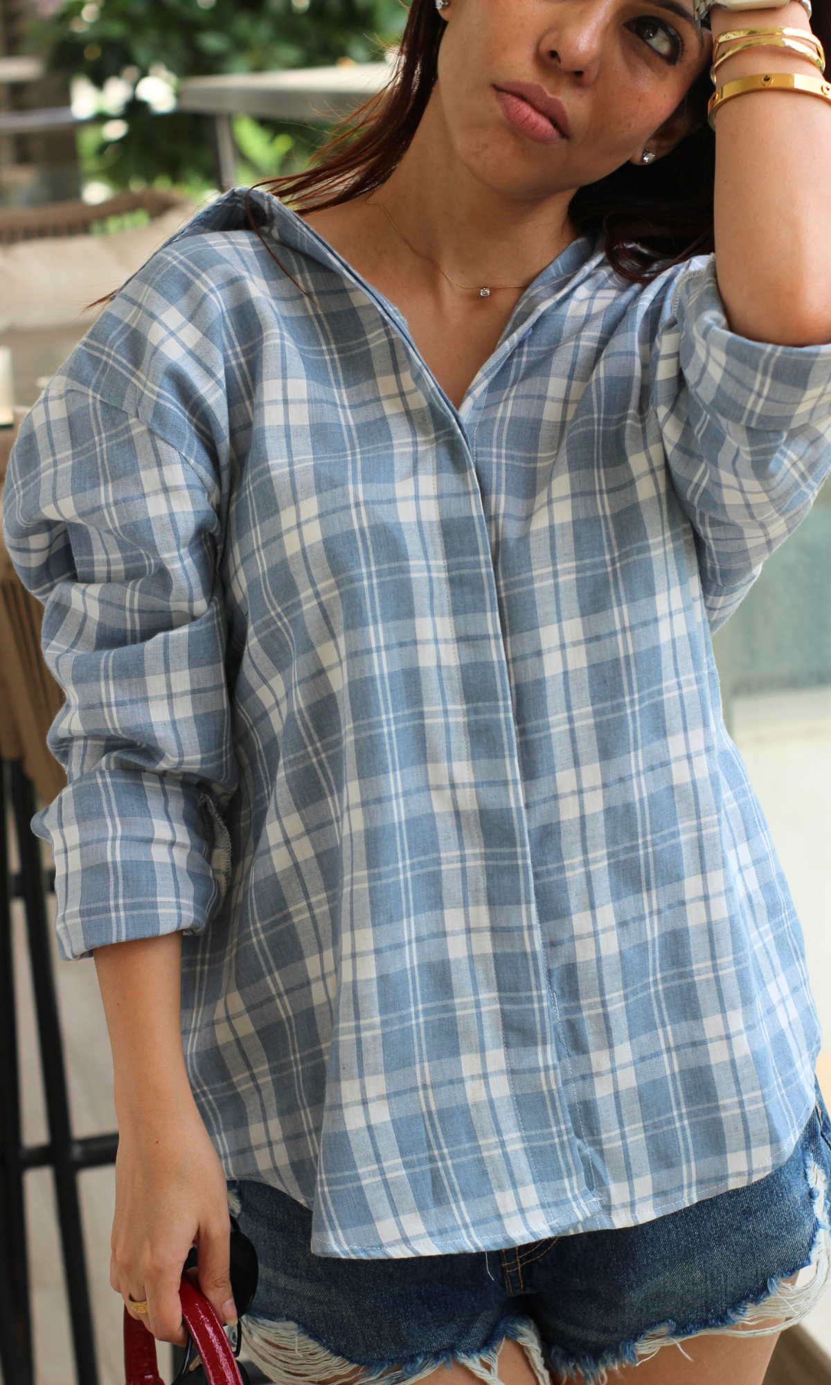 Breezy summer balcony look featuring a soft blue checkered shirt and ripped denim shorts styled with white flats and minimal accessories.