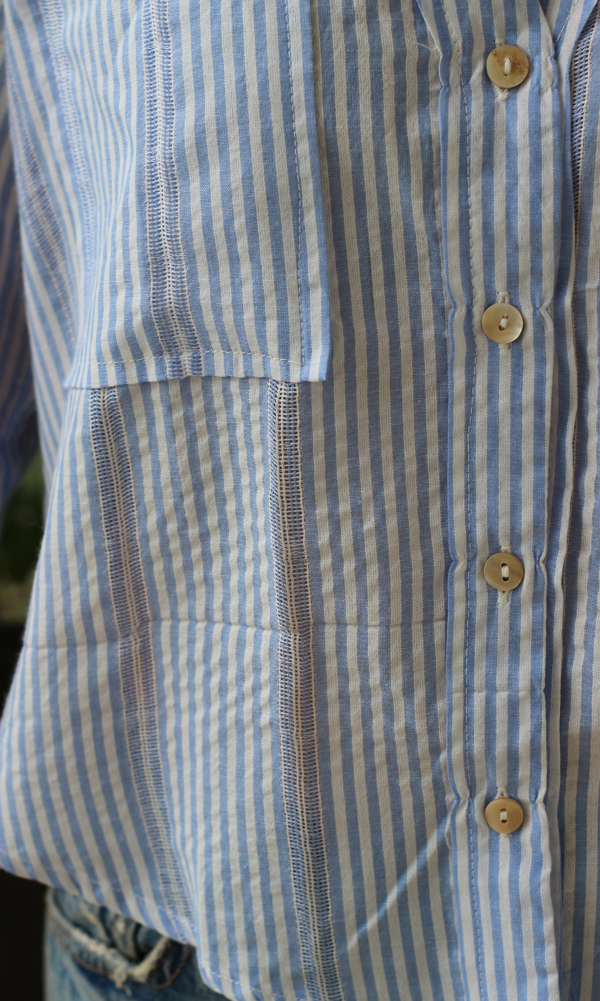 Close-up of blue striped cotton shirt with buttons and front pocket detail.