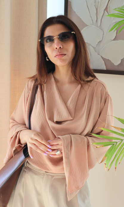 Fashionable dusky pink top featuring a cowl neckline and elegant slit sleeves, paired with casual bottoms.