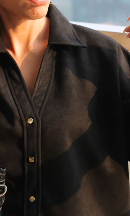 Close-up view of black suede shirt showing metallic button detailing and soft textured fabric finish.