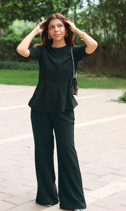 Woman wearing a black peplum top paired with matching black wide-leg trousers and minimal accessories for a chic monochrome look.