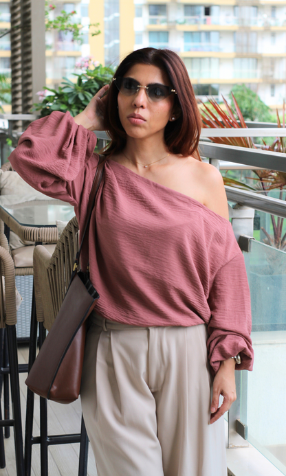 Mauve off-shoulder blouse with cream pleated pants and brown shoulder bag, styled with sunglasses.