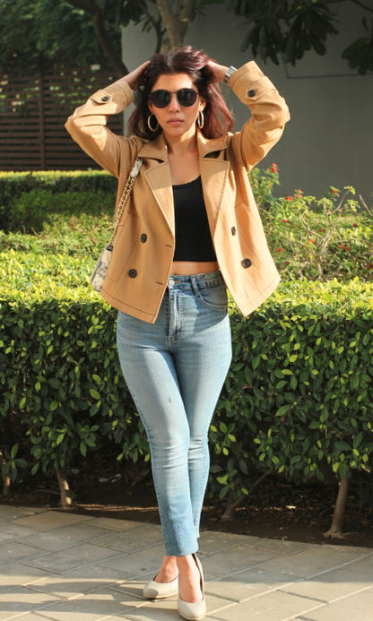 Woman wearing a tan thread detail trench coat styled with denim jeans and heels