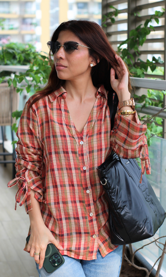Rust checkered shirt with gathered sleeves, paired with denim and a black puffer bag.