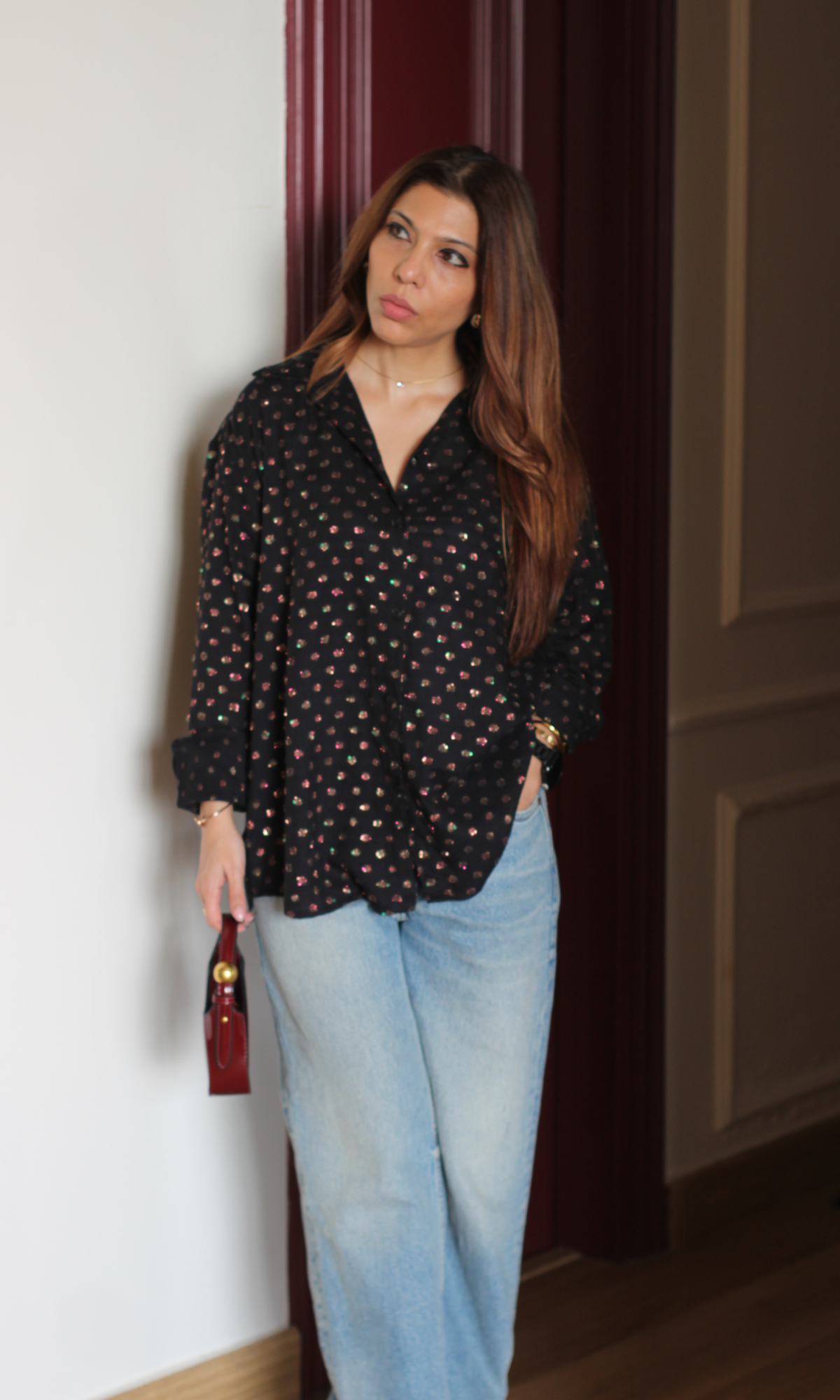 Black lurex flowing shirt styled casually with light denim jeans on balcony setting.