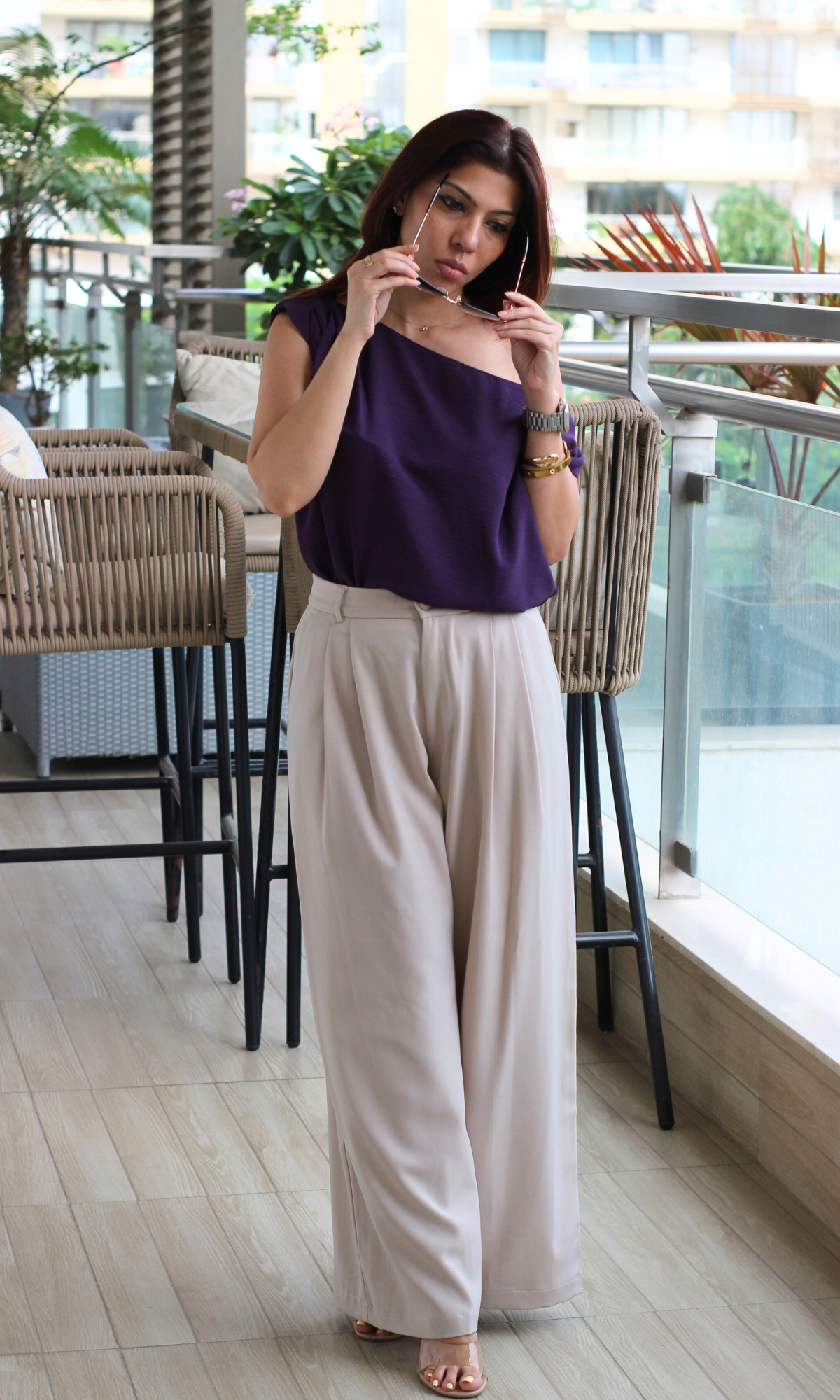 Woman wearing a purple top and beige pants in an outdoor setting.