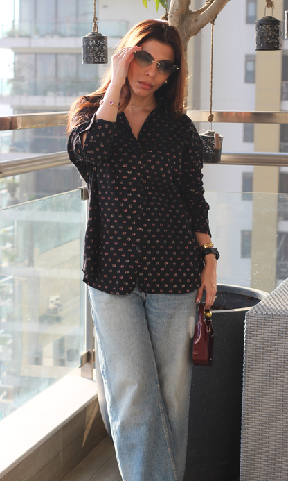 Woman wearing a black lurex flowing shirt with subtle shimmer, styled with blue jeans and sunglasses.