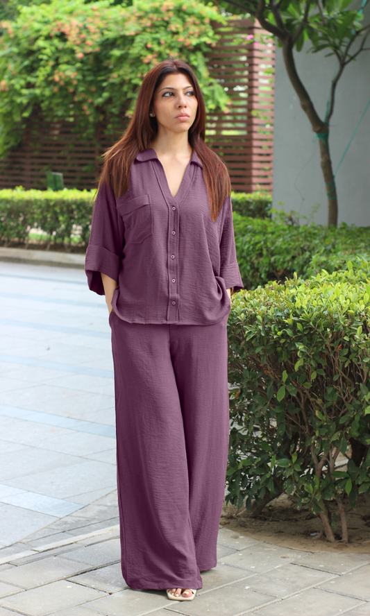 Relaxed plum lounge set worn with heels, shot in an outdoor garden setting.
