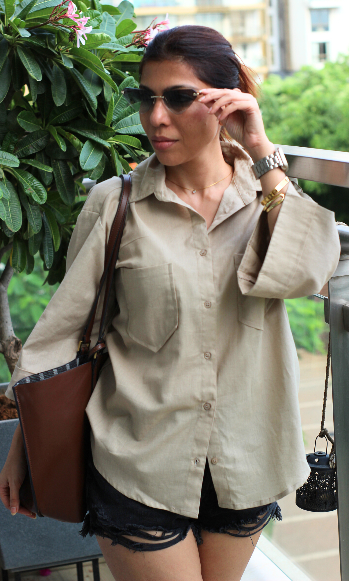 Casual summer outfit featuring an oversized beige shirt with front pockets, styled with distressed black shorts.