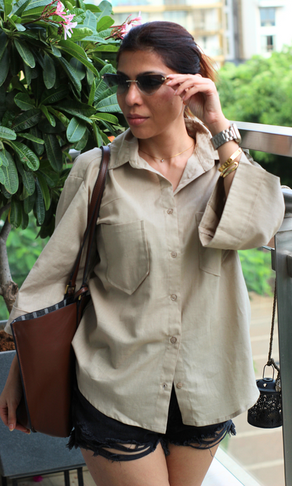 Casual summer outfit featuring an oversized beige shirt with front pockets, styled with distressed black shorts.