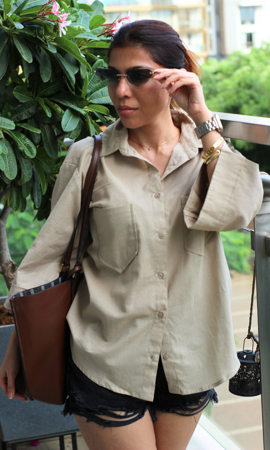 Casual summer outfit featuring an oversized beige shirt with front pockets, styled with distressed black shorts.